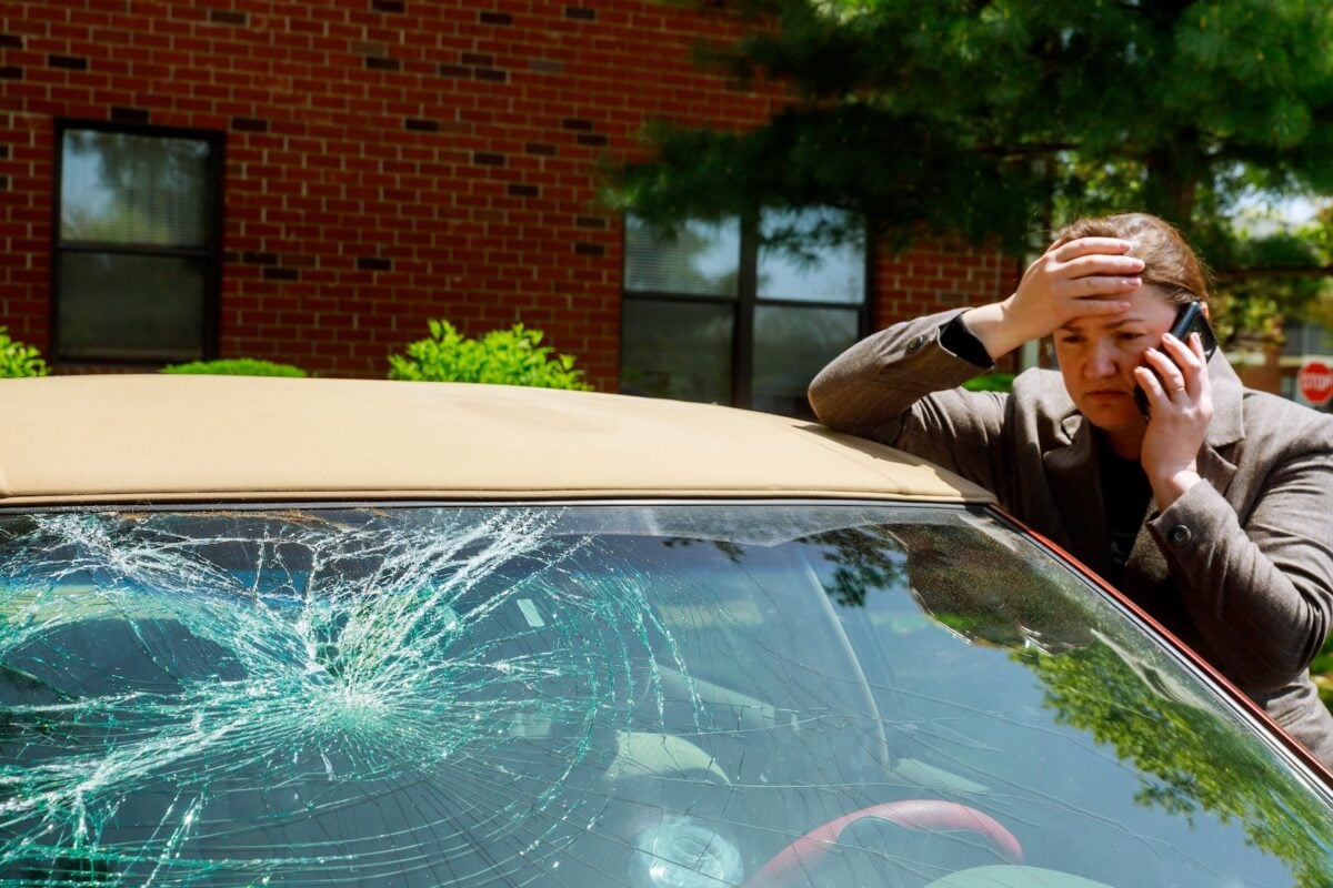 Woman making a phone call next to broken windshield after a car accident.